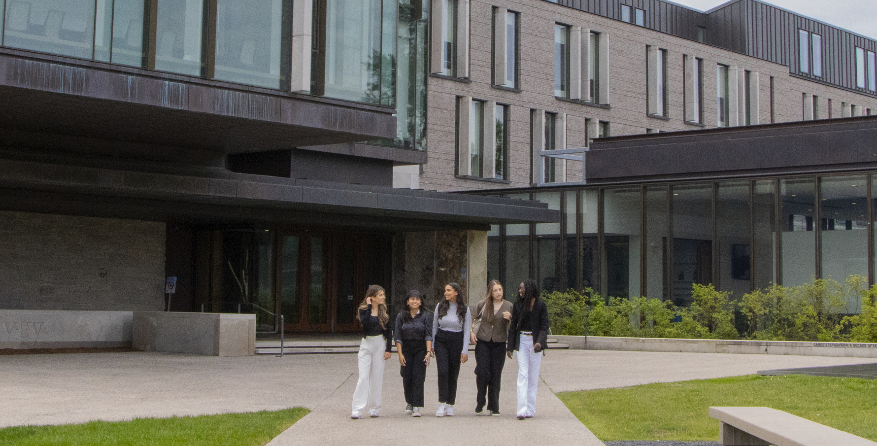 Five students walking together outside a campus building
