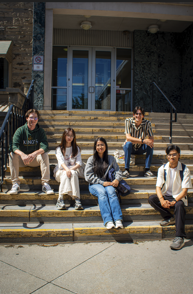 Six students sitting together on the front steps of a King’s building